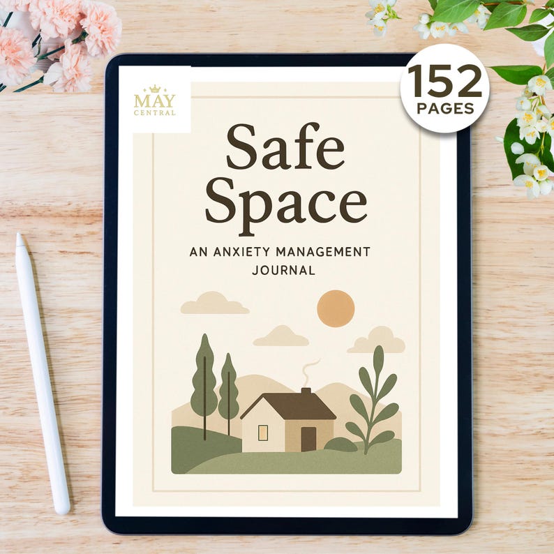 May include: A digital tablet displaying a journal titled "Safe Space: An Anxiety Management Journal." The cover features a house illustration, trees, clouds, and a sun. The journal has 152 pages. A white stylus pen rests on the wooden surface.