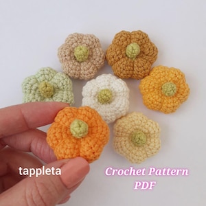 Puede incluir: Un conjunto de flores de ganchillo hechas a mano en varios colores, como naranja, amarillo, verde y beige. Cada flor tiene un diseño texturizado con un centro verde. La imagen incluye el texto "tappleta" y "Crochet Pattern PDF".