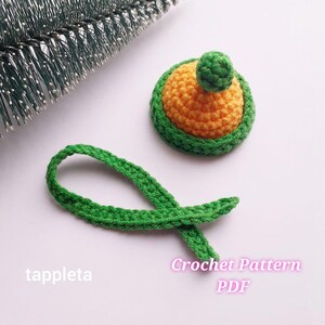 Peut inclure: Un chapeau d'avocat crocheté à la main, avec une tige verte et un pompon vert sur le dessus. Le chapeau est orange et vert. L'image comprend également une tige crochetée verte et le texte "tappleta" et "Crochet Pattern PDF".