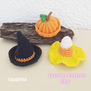 Può includere: Decorazioni di Halloween all'uncinetto. L'immagine presenta un cappello da strega nero con dettagli arancioni, una zucca arancione con un gambo verde e un cappello a forma di caramella. È visibile anche il testo "tappleta" e "Crochet Pattern PDF".