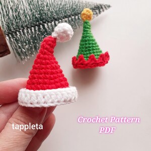 May include: Two miniature crochet Christmas hats. One is red with a white brim and pom-pom, resembling a Santa hat. The other is green with a red scalloped brim and a yellow top. The image includes the text "Crochet Pattern PDF".
