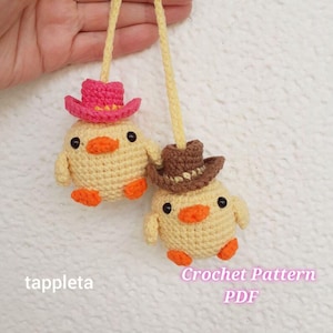 May include: Two crocheted yellow chick ornaments with orange beaks and feet, each wearing a cowboy hat. One hat is pink, the other is brown. The text "tappleta" and "Crochet Pattern PDF" are visible.
