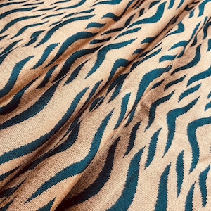 May include: Close-up of a fabric with a tiger stripe pattern. The fabric has a tan background with teal blue stripes. The fabric is folded, creating shadows and texture.