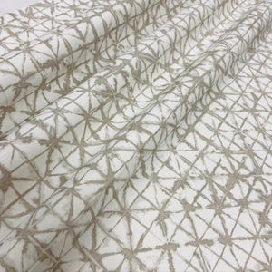 Pode incluir: Tecido branco com um padrão geométrico repetitivo em tons de bege e castanho. O padrão consiste em formas interligadas, criando uma aparência texturizada. O tecido é provavelmente adequado para estofados ou projetos de decoração de casa.