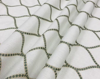 May include: White fabric with a repeating geometric pattern. The pattern consists of interconnected, curved lines with small, evenly spaced dots in a muted green color. The fabric is folded, showing texture and depth.