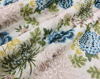 May include: Floral fabric with a cream background. The fabric features large, detailed flowers in shades of blue, pink, yellow, and green. The design includes chrysanthemums and other floral elements, creating a textured, botanical pattern.
