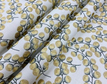 May include: White fabric with a repeating pattern of gold-colored, circular leaf clusters and dark gray stems. The fabric is folded, showing the texture and depth of the design. The leaves have a textured, embroidered appearance.