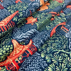 May include: Dark blue fabric with a repeating pattern of orange pagodas, trees, and foliage. The design includes red accents and a variety of green and white leaves. The fabric is folded, showing the texture and depth of the material.