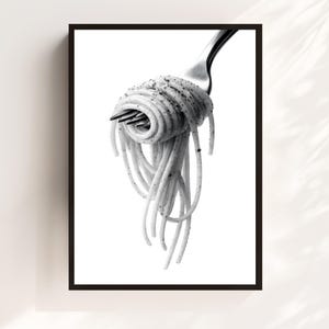 May include: Black and white framed print featuring a close-up of spaghetti twirled around a fork. The pasta is speckled with herbs and spices, with strands cascading down. The image is set against a bright white background.