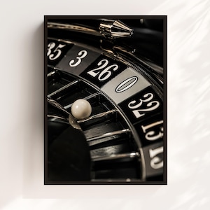 May include: A close-up view of a black roulette wheel featuring white numbers including 35, 3, 26, 0, and 32. A small white ball rests in the slot for the number 3. The wheel has metallic silver dividers and a polished black surface with high contrast.