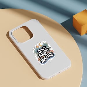 Może przedstawiać: Białe etui na telefon z naklejką z napisem "Don't Forget to Breathe". Naklejka przedstawia słońce, księżyc i fale w stylu retro. Etui leży na jasnobrązowej powierzchni.