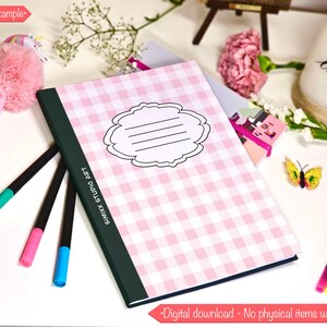 Könnte beinhalten: Ein Notizbuch mit rosa-weißem Vichy-Karo-Muster und einem dekorativen Etikett, umgeben von bunten Stiften und einem rosa Pompon-Stift. Der Buchrücken ist dunkelgrün mit dem Text "SIMIXX STUDIO ART". Eine Kerze mit dem Wort "love" ist ebenfalls zu sehen.