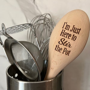 May include: A wooden spoon with the text "I'm Just Here to Stir the Pot" engraved on it. The spoon is in a metal utensil holder with other kitchen tools.