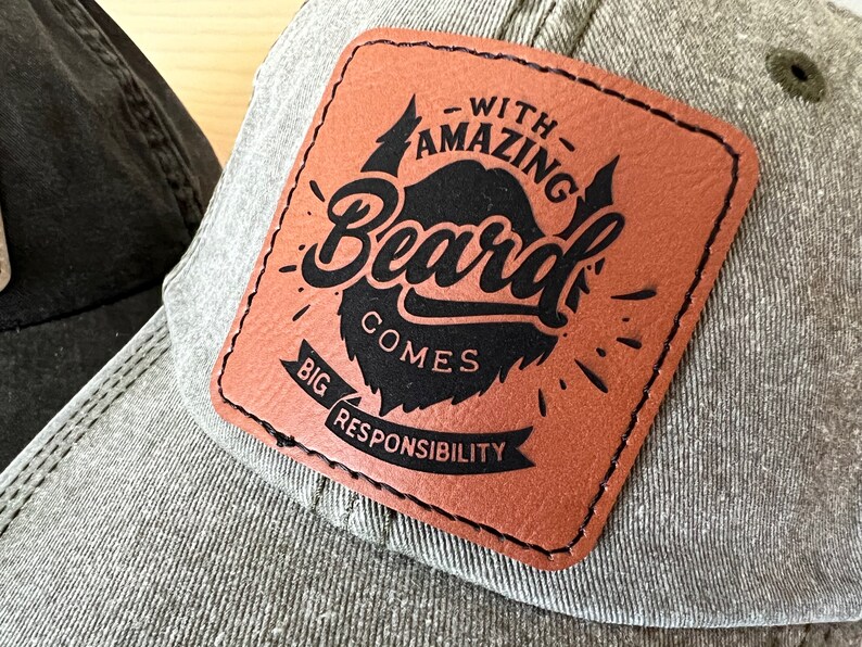 Peut inclure: Un patch en cuir marron avec des coutures noires et du texte qui dit "With Amazing Beard Comes Big Responsibility". Le patch est fix&eacute; &agrave; une casquette de baseball grise.