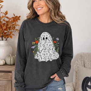 May include: A charcoal gray long-sleeve crewneck shirt featuring a central graphic of a white lace-patterned ghost surrounded by colorful wildflowers including red, orange, yellow, and purple blossoms with green stems and leaves.