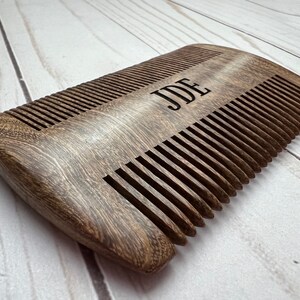Peut inclure: Un peigne en bois brun fonc&eacute; avec le nom "JDE" grav&eacute; sur le dessus. Le peigne a une forme incurv&eacute;e et est fait de bois naturel.