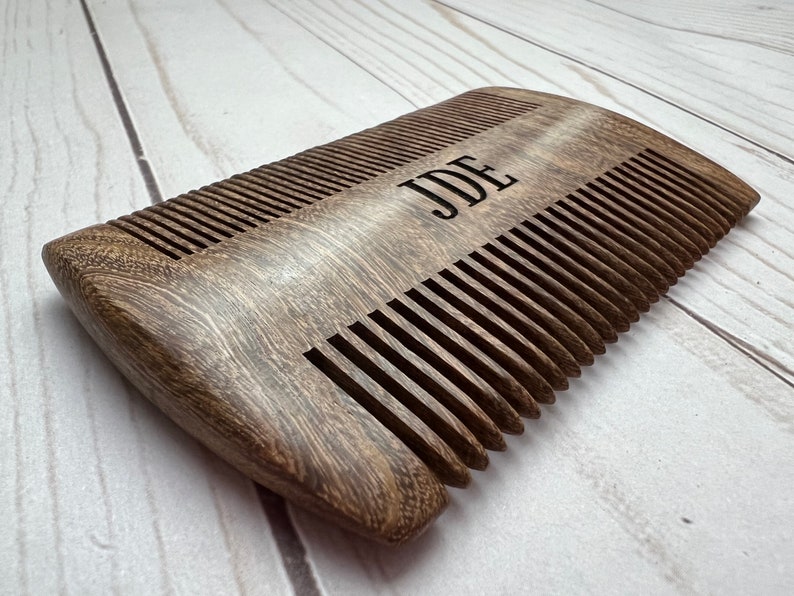 Peut inclure: Un peigne en bois brun fonc&eacute; avec le nom "JDE" grav&eacute; sur le dessus. Le peigne a une forme incurv&eacute;e et est fait de bois naturel.