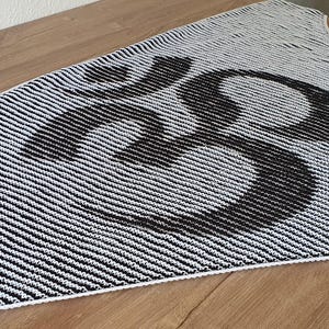 May include: A black and white knitted shawl with a large, stylized "23" design. The shawl features a striped pattern with a white border. The design is likely handmade and suitable for cool weather.