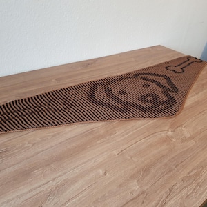 May include: A brown and black dog-themed table runner. The runner features a dog face and bone design at one end. The runner is made of a striped fabric and is placed on a wooden table. The runner is approximately 60 inches long.