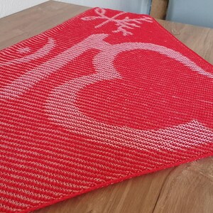 May include: A red knitted scarf with a white snowflake design. The scarf is made of a soft, textured yarn and has a fringed edge.