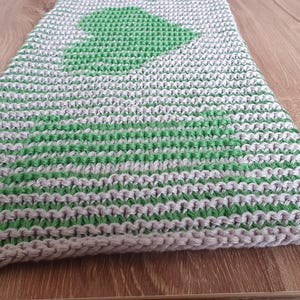 May include: A knitted scarf with a green tree design on a white and gray background. The scarf is made of a soft, textured yarn and has a simple, classic design. The scarf is approximately 60 inches long.
