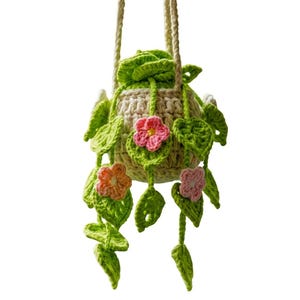 Puede incluir: Un macetero colgante de ganchillo hecho a mano con una maceta beige, adornado con hojas verdes y flores rosas y naranjas. El macetero está suspendido por una cuerda de color crema, perfecto para añadir un toque de naturaleza a cualquier espacio.