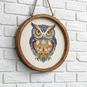 May include: Round wooden framed wall art featuring a detailed owl illustration. The owl is depicted with intricate patterns in shades of blue, orange, and yellow. The artwork is suspended by a natural rope.