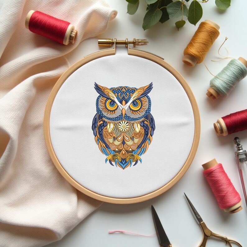 May include: A colorful owl embroidery design in a wooden hoop. The owl features intricate patterns in shades of blue, gold, and orange. Spools of red, yellow, and green thread, along with scissors, are arranged around the hoop, suggesting a craft project.