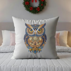 May include: White square pillow featuring a detailed owl design. The owl has intricate patterns in shades of blue, gold, and orange. The pillow is placed on a bed with a white comforter, with a Christmas wreath in the background.