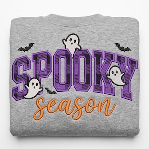 May include: A heather gray sweatshirt featuring embroidered text that reads SPOOKY in large purple and black plaid block letters and season in orange cursive script. The design includes three white ghosts and three black bats.