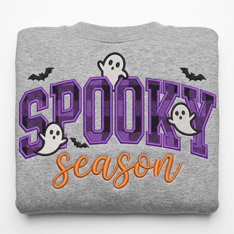 May include: A heather gray sweatshirt featuring embroidered text that reads SPOOKY in large purple and black plaid block letters and season in orange cursive script. The design includes three white ghosts and three black bats.