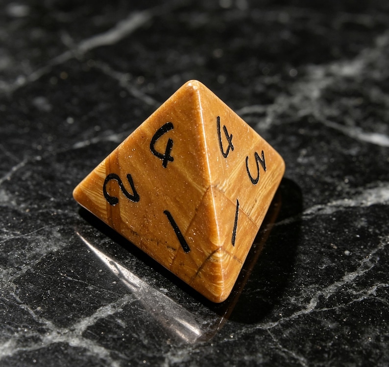 May include: A four-sided pyramid-shaped die crafted from a tan, wood-grained material. The faces of the die feature black ink numbers, including a visible 1, 2, 3, and 4, arranged in a standard numerical sequence for this type of gaming piece.