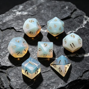 May include: A set of seven polyhedral dice made of a translucent, milky white material with an iridescent blue glow. Each die features engraved numbers filled with gold ink, including a d20, d12, d10, d8, d6, d4, and a percentile die.