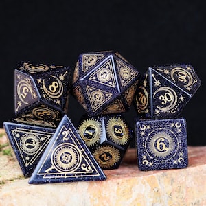 May include: A set of seven polyhedral dice in a deep blue color with gold-colored markings. The dice are arranged on a stone surface against a dark background. Each die features intricate designs and numbers, suitable for tabletop gaming.