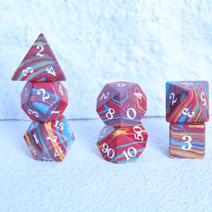 May include: A set of multi-coloured polyhedral dice with a marbled effect in red, blue, and yellow. The dice are arranged to display their different shapes and numbers, ideal for tabletop gaming.