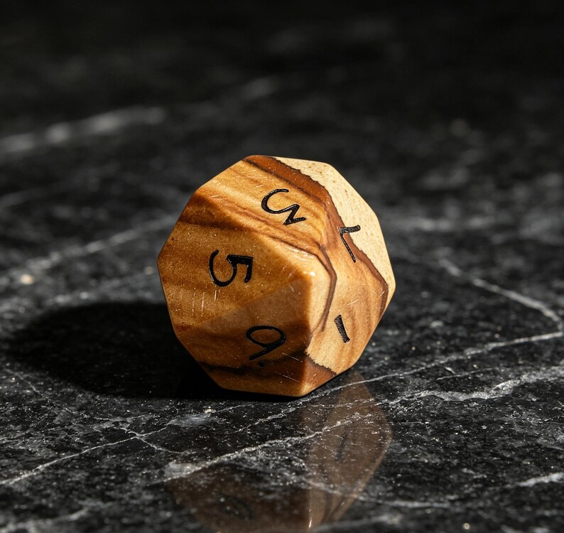 May include: A multi-faceted wooden die featuring a natural light and dark brown wood grain pattern. The die has black engraved numbers visible on its surface, including the digits 5 and 9, along with other partial numerical markings.