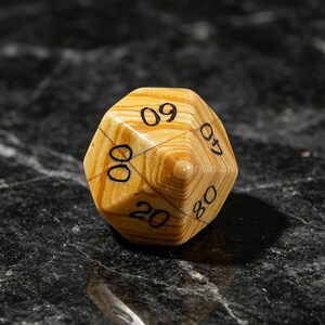 May include: A ten-sided die featuring a light brown and tan wood grain pattern with black engraved numbers. The visible faces display the numbers 09, 07, 80, 20, and 00. The die has a pointed top and a smooth, polished finish throughout.