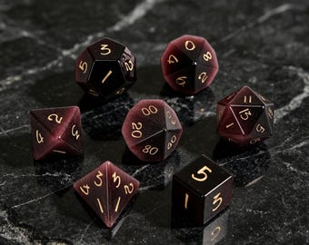 May include: A set of seven polyhedral dice crafted from a deep purple, chatoyant material with a shimmering cat's eye effect. Each die features engraved numbers filled with gold-colored ink, including a d20, d12, d10, d8, d6, d4, and a percentile die.