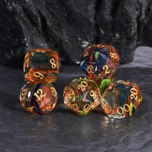 Puede incluir: Un conjunto de seis dados poliédricos con un aspecto colorido y veteado. Los dados presentan una mezcla de tonos naranja, rojo, azul y verde con números dorados. Diseñados para juegos de rol de mesa.