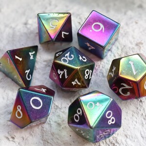 May include: A set of seven iridescent polyhedral dice with white numbering. The dice have a metallic finish with colors that shift from purple to gold. The dice are used for tabletop role-playing games.