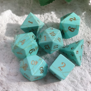 May include: A collection of seven multi-sided dice, including a d4, d6, d8, d10, d12, d20, and a percentile die. The dice are turquoise with gold numbering and veining. Suitable for role-playing games.