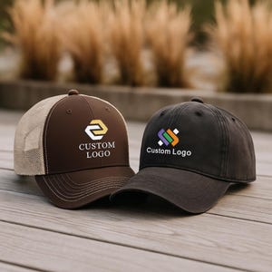 May include: Two baseball caps with custom logos. One is brown with a tan mesh back and a white logo. The other is dark gray with a colorful logo. Both caps have the text "Custom Logo".