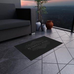 Può includere: Un tappetino rettangolare nero con un design grafico centrale chiaro e intricato, caratterizzato da motivi ornamentali simmetrici e dalla scritta stilizzata "HIMHER" in un carattere decorativo audace su uno sfondo scuro e uniforme.