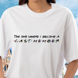 May include: White t-shirt with the text "The One Where I Become A Cast Member" in black with colorful dots.