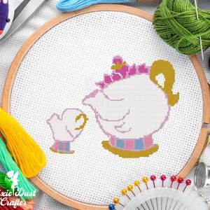 May include: A cross-stitch embroidery hoop featuring a white teapot and teacup design with pink, blue, and gold accents. The design is set against a white fabric background, surrounded by colorful embroidery floss and sewing supplies.