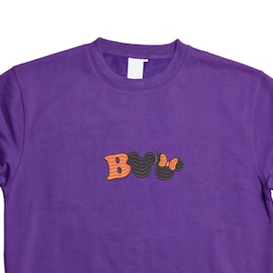 May include: Purple sweatshirt with a black and orange embroidered "Boo" design.