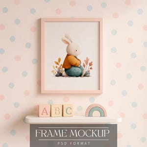 May include: A framed watercolor print of a bunny wearing an orange jacket and blue pants. The pink frame is mounted on a wall with a polka dot pattern. Below the frame is a shelf with wooden blocks and a rainbow.