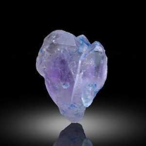 May include: A translucent amethyst crystal cluster with a deep purple centre and light blue edges. The crystal has a reflective surface, and small blue inclusions are visible throughout. The background is black.