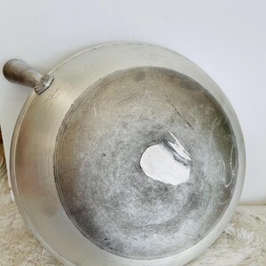 Puede incluir: Un wok de aluminio plateado con un mango. El wok tiene un aspecto desgastado, con algunos ara&ntilde;azos y decoloraci&oacute;n.