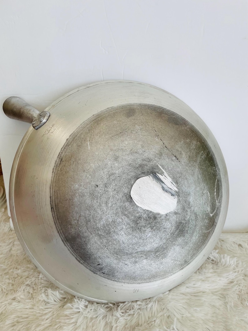 Puede incluir: Un wok de aluminio plateado con un mango. El wok tiene un aspecto desgastado, con algunos ara&ntilde;azos y decoloraci&oacute;n.